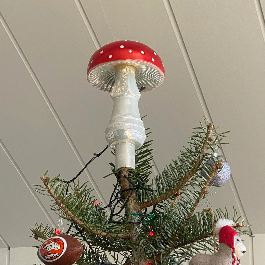 Decorative mushroom light bulb hanging on a Christmas tree with ornaments.